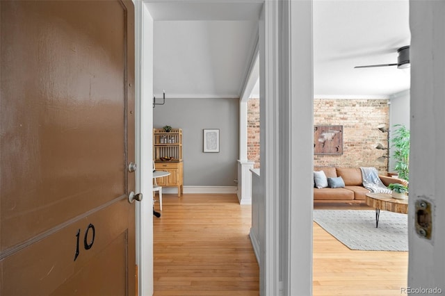 hallway with ornamental molding, brick wall, light wood finished floors, and baseboards