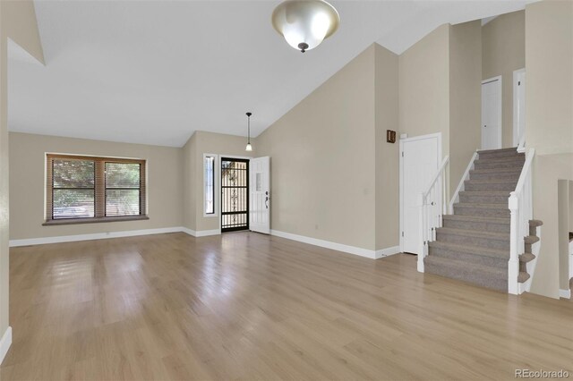 14463 E Wagon Trail Pl, Aurora, CO 80015 - unfurnished living room with high vaulted ceiling, light wood finished floors, and stairs