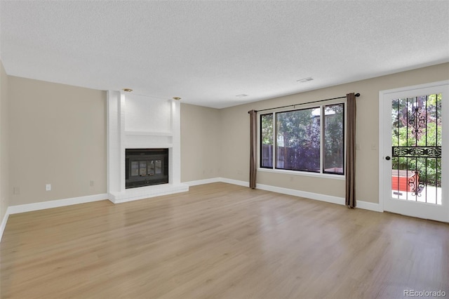 14463 E Wagon Trail Pl, Aurora, CO 80015 - unfurnished living room with a textured ceiling, light wood-style flooring, healthy amount of natural light, and a fireplace
