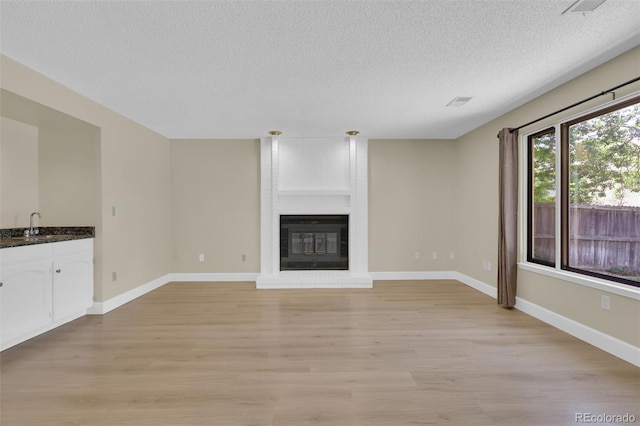 14463 E Wagon Trail Pl, Aurora, CO 80015 - unfurnished living room with a textured ceiling, light wood-style floors, and a brick fireplace