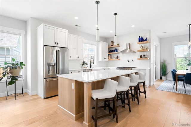 8357 W 68th Ln, Arvada, CO 80004 - kitchen with high end fridge, open shelves, wall chimney exhaust hood, a center island, and light wood-style flooring