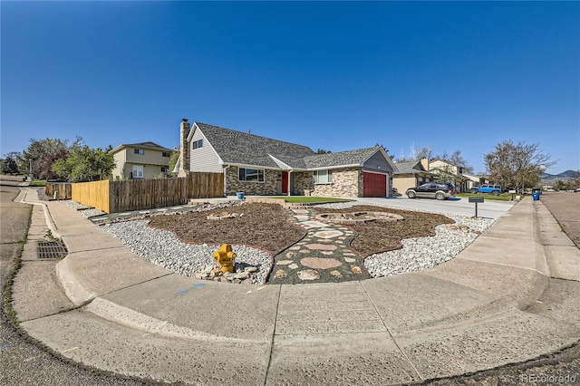 view of side of home featuring a residential view, a garage, fence, concrete driveway, and stone siding