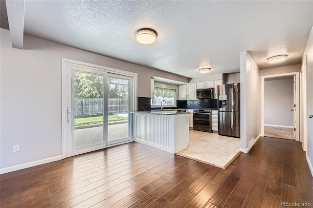 kitchen with a peninsula, baseboards, white cabinets, tasteful backsplash, and appliances with stainless steel finishes