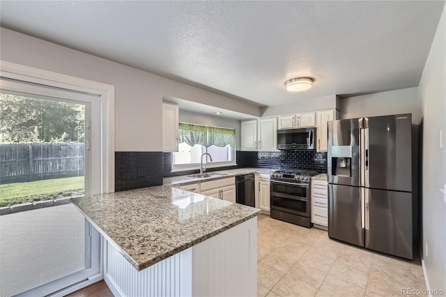 kitchen featuring decorative backsplash, a peninsula, light stone counters, a sink, and stainless steel appliances