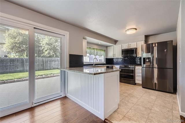kitchen with a sink, stainless steel appliances, white cabinetry, a peninsula, and decorative backsplash