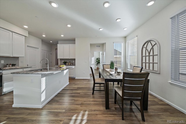 kitchen with a kitchen island with sink, dark stone counters, dark hardwood / wood-style floors, white cabinets, and sink