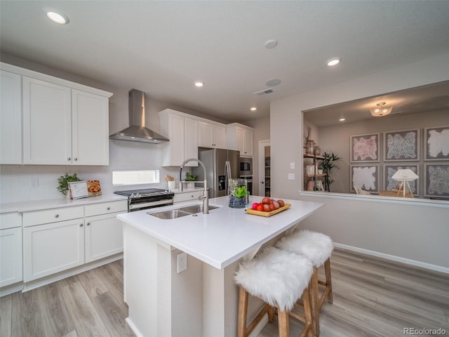 kitchen featuring wall chimney exhaust hood, a breakfast bar area, white cabinetry, a center island with sink, and appliances with stainless steel finishes