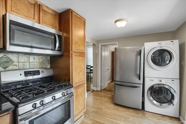 2415 Chase St, Edgewater, CO 80214 - kitchen featuring stainless steel appliances, stacked washer / drying machine, brown cabinets, light wood-type flooring, and dark countertops