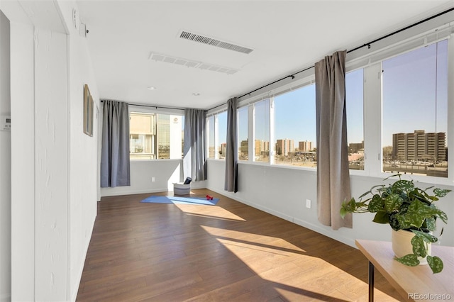 exercise area with visible vents, a view of city, baseboards, and wood finished floors