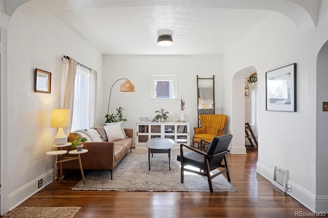 living room with dark wood-type flooring, arched walkways, visible vents, and baseboards