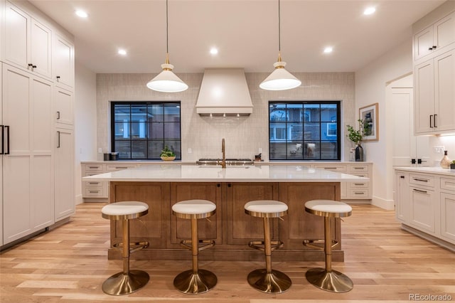 kitchen with light countertops, premium range hood, a kitchen bar, and light wood-style flooring