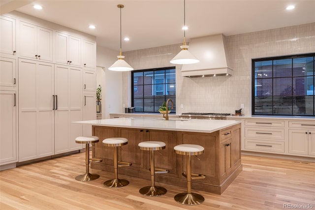 kitchen with a sink, light countertops, light wood-type flooring, and custom exhaust hood