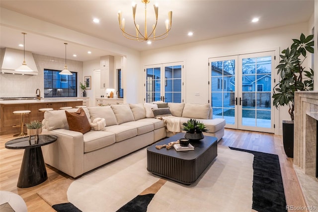 living room with a chandelier, recessed lighting, a high end fireplace, light wood-style floors, and french doors