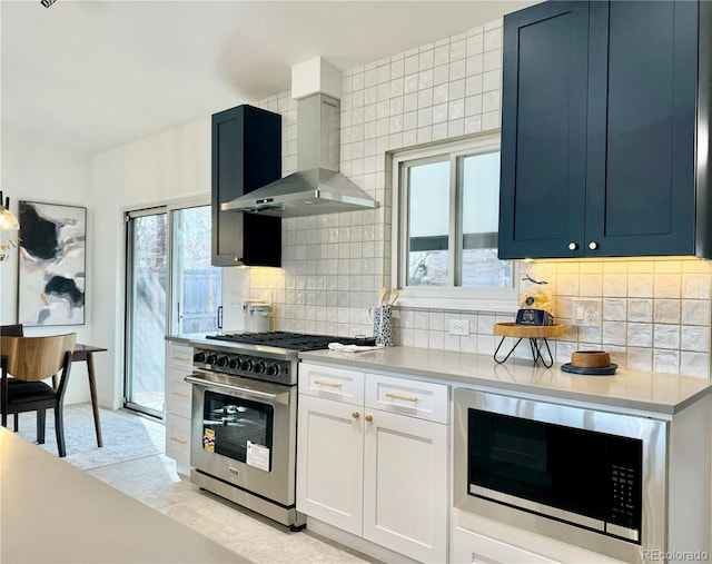 kitchen with blue cabinets, white cabinetry, appliances with stainless steel finishes, wall chimney range hood, and backsplash