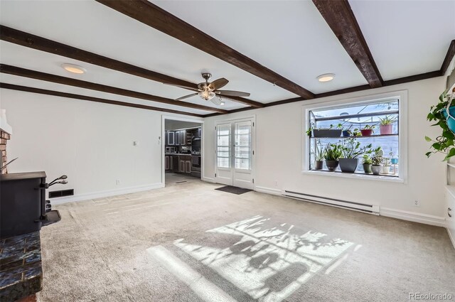 unfurnished living room with beamed ceiling, light colored carpet, a wood stove, and baseboard heating