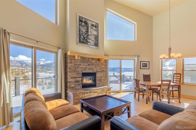 living room with a high ceiling, light wood-style floors, a mountain view, a stone fireplace, and a chandelier