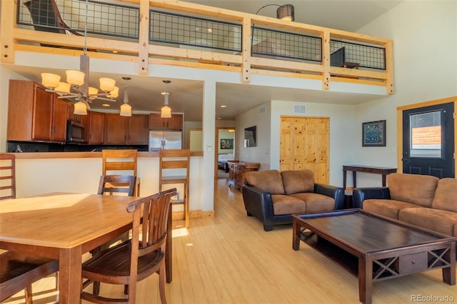 living room featuring visible vents, a high ceiling, light wood-style flooring, and a notable chandelier