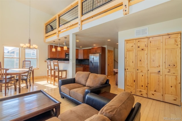 living room featuring a chandelier, a high ceiling, visible vents, baseboards, and light wood-style floors