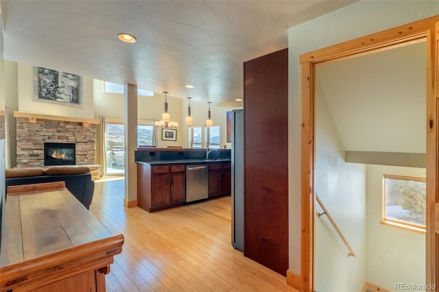 kitchen with light wood-style flooring, a fireplace, stainless steel dishwasher, fridge, and dark countertops