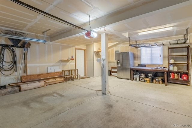 garage featuring stainless steel refrigerator with ice dispenser, a workshop area, and a garage door opener