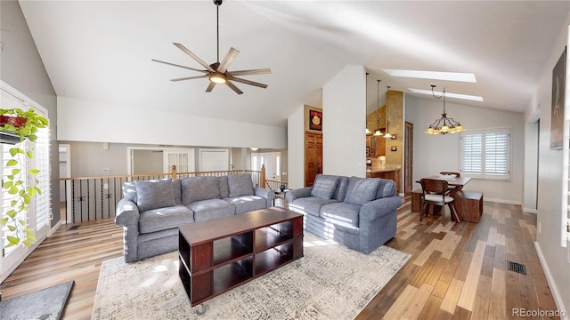 living area with a skylight, visible vents, light wood-style flooring, high vaulted ceiling, and ceiling fan with notable chandelier