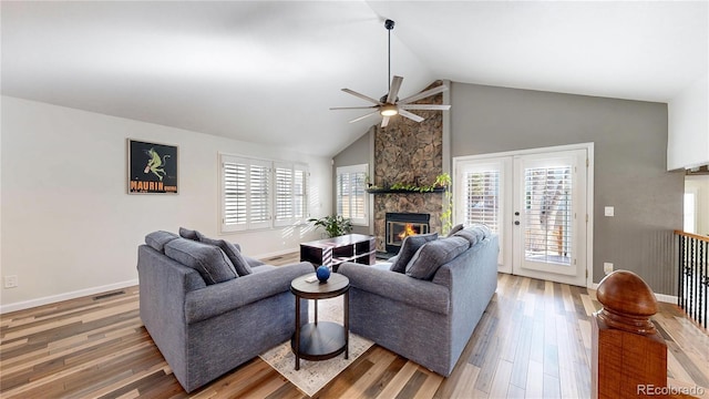 living area with ceiling fan, high vaulted ceiling, wood finished floors, and a stone fireplace