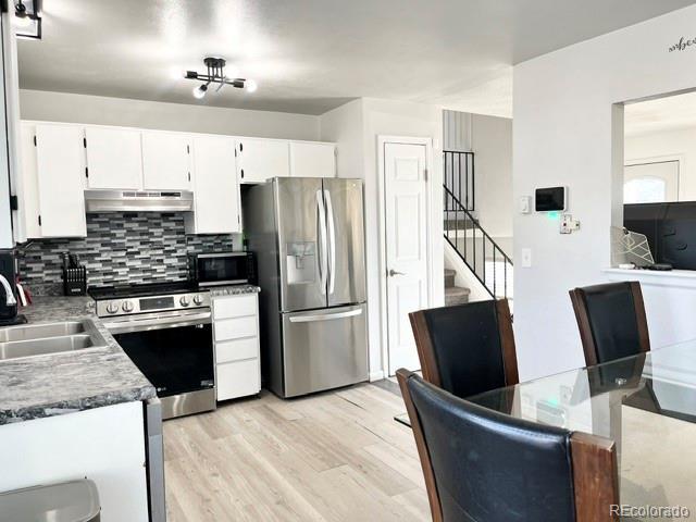 17413 E Louisiana Ave, Aurora, CO 80017 - kitchen with appliances with stainless steel finishes, under cabinet range hood, a sink, decorative backsplash, and light wood-type flooring
