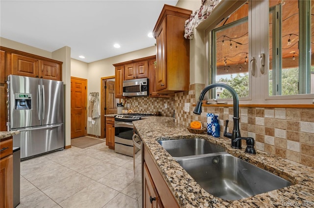 kitchen with backsplash, light stone counters, sink, and appliances with stainless steel finishes