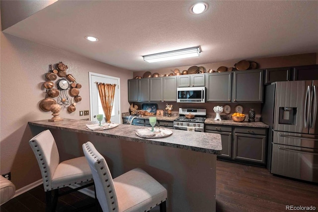 12242 Bannock Cir Unit D, Denver, CO 80234 - kitchen with stainless steel appliances, a kitchen bar, gray cabinets, dark wood-style floors, and a textured ceiling