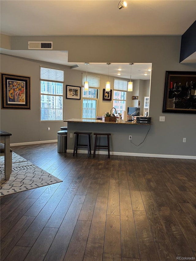 kitchen featuring decorative light fixtures, dark wood finished floors, a breakfast bar area, visible vents, and a peninsula