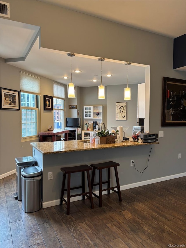 kitchen featuring a peninsula, dark wood-type flooring, visible vents, a kitchen bar, and decorative light fixtures
