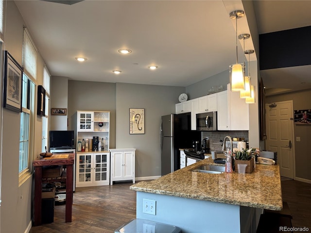 kitchen with dark wood-style floors, stainless steel appliances, hanging light fixtures, white cabinetry, and a sink