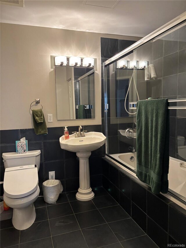 bathroom with tile walls, tiled shower / bath, toilet, a sink, and tile patterned floors