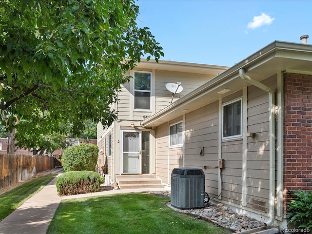 back of house featuring a lawn, entry steps, central AC, fence, and brick siding