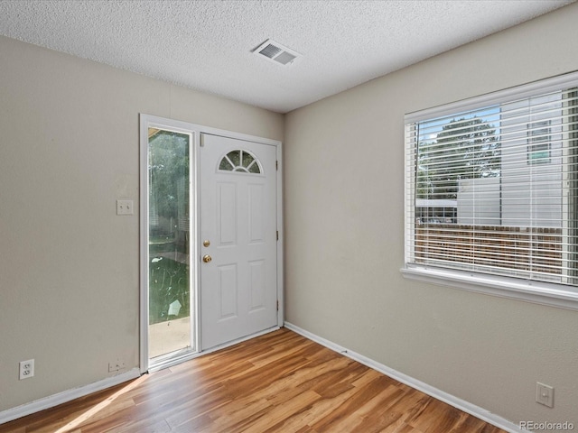 foyer entrance with light wood-style flooring, baseboards, visible vents, and a textured ceiling