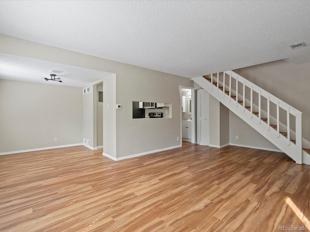 unfurnished living room featuring baseboards, visible vents, stairs, a textured ceiling, and light wood-type flooring