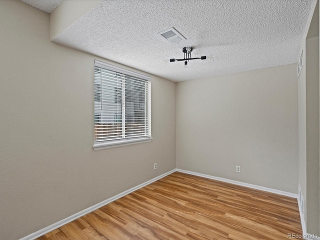 empty room with a textured ceiling, wood finished floors, visible vents, and baseboards