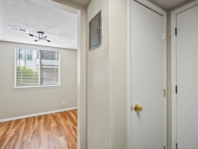 hallway featuring baseboards, wood finished floors, visible vents, and a textured ceiling