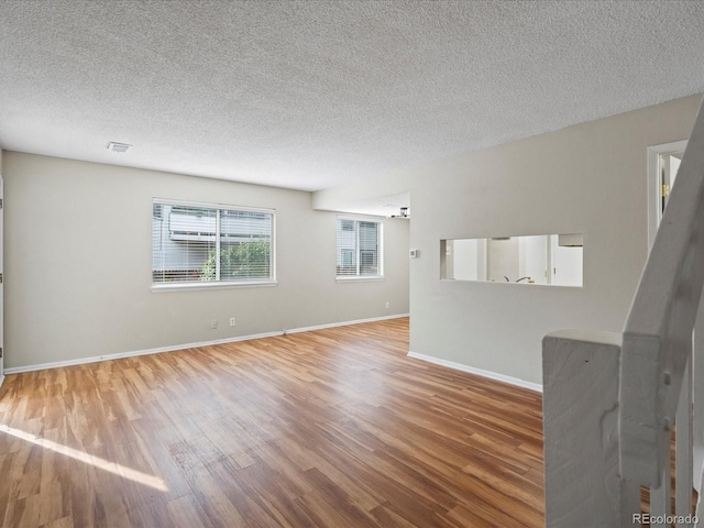 unfurnished living room with visible vents, baseboards, a textured ceiling, and wood finished floors