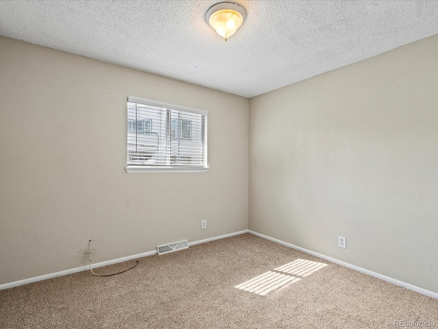 empty room featuring carpet flooring, a textured ceiling, baseboards, and visible vents