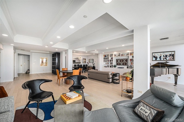 living area with a raised ceiling, ornamental molding, light wood-style floors, built in shelves, and recessed lighting