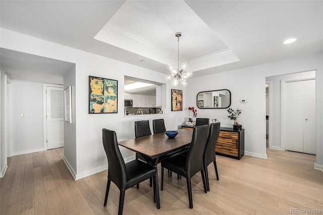 dining space featuring crown molding, a raised ceiling, an inviting chandelier, light wood-style floors, and baseboards