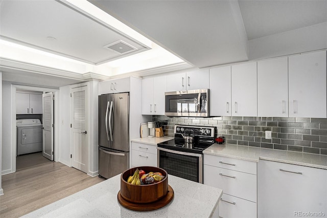 kitchen with light wood-style flooring, white cabinets, appliances with stainless steel finishes, washer / clothes dryer, and tasteful backsplash