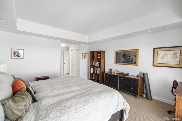 bedroom featuring light carpet, a tray ceiling, and baseboards