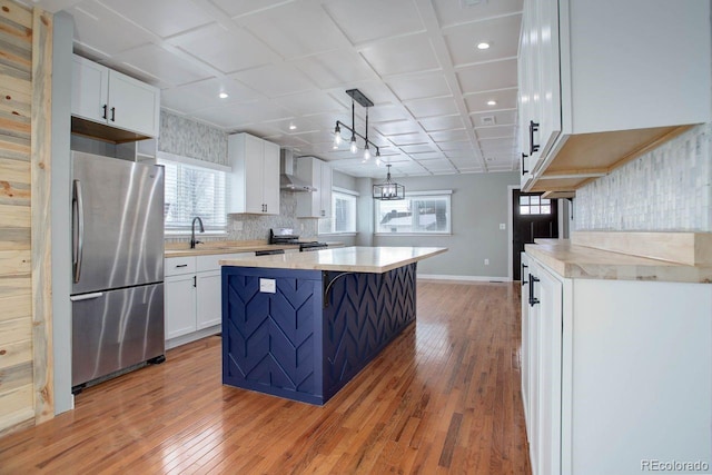 kitchen with a center island, appliances with stainless steel finishes, white cabinetry, decorative light fixtures, and wall chimney exhaust hood