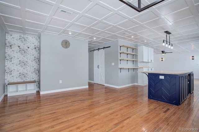 unfurnished living room featuring ceiling fan, coffered ceiling, a barn door, and light wood-type flooring