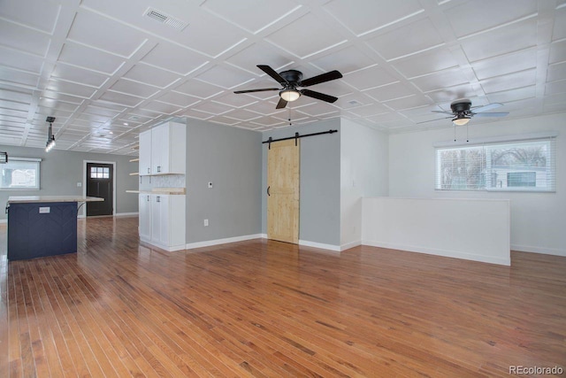 unfurnished living room with ceiling fan, hardwood / wood-style floors, a barn door, and coffered ceiling