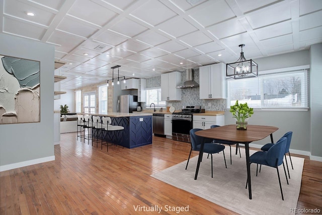 dining room featuring coffered ceiling, light hardwood / wood-style flooring, and an inviting chandelier