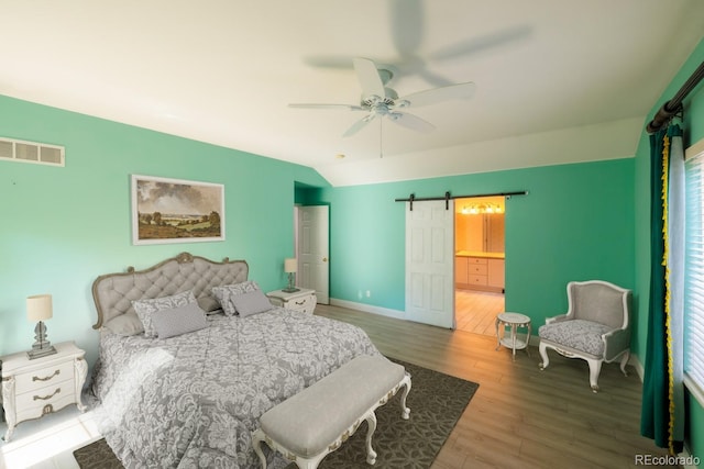 bedroom featuring vaulted ceiling, ensuite bathroom, hardwood / wood-style flooring, ceiling fan, and a barn door