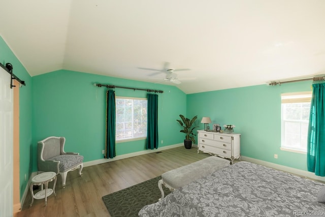 bedroom with ceiling fan, a barn door, light hardwood / wood-style floors, and vaulted ceiling